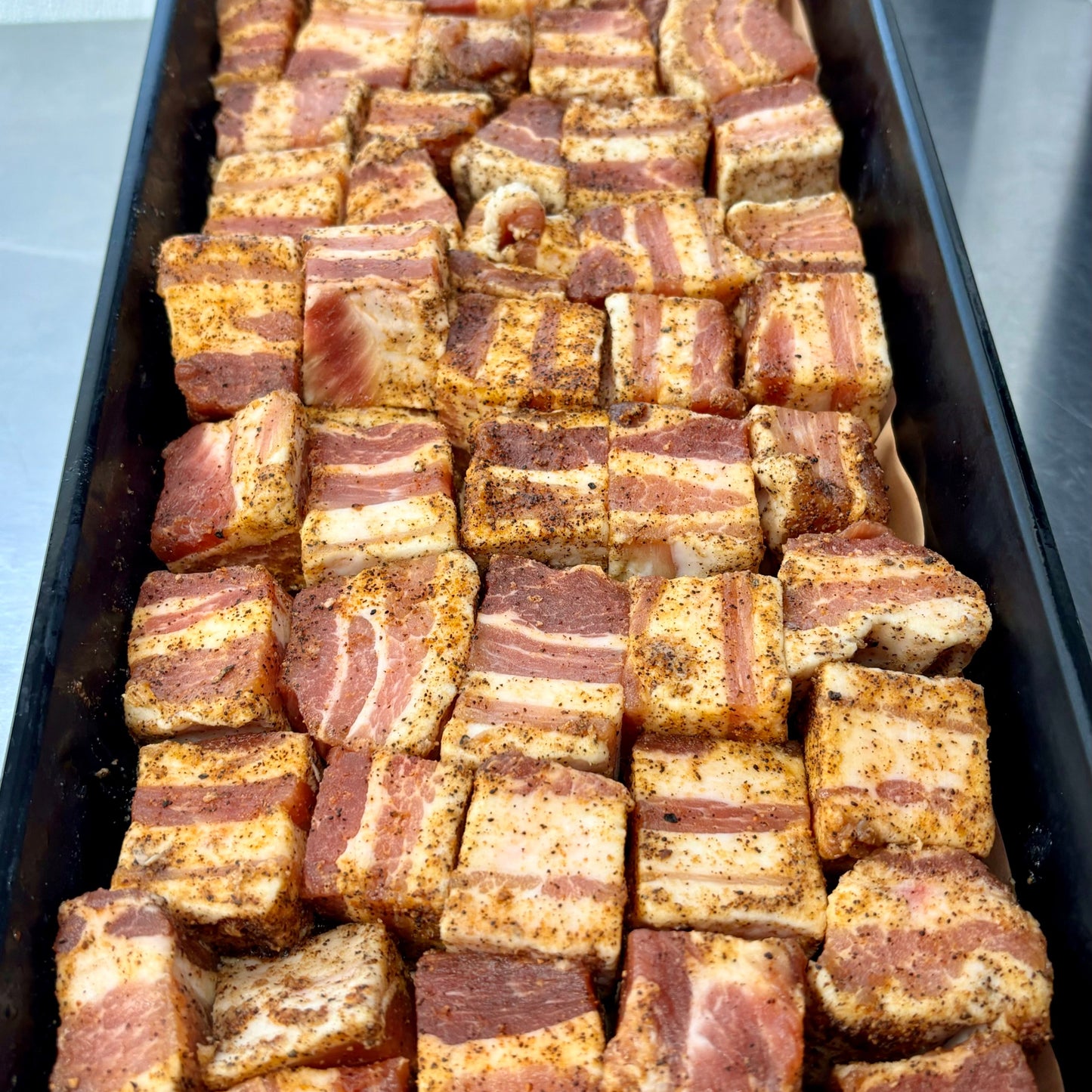 seasoned pork belly cubes in a black butcher tray